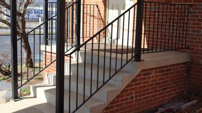 Black vertical-bar railing on concrete steps at a brick entrance