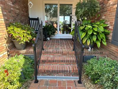 Black vertical-bar railings flanking brick steps surrounded by potted plants