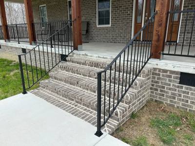 Black vertical-bar railings on wide brick steps to a covered porch