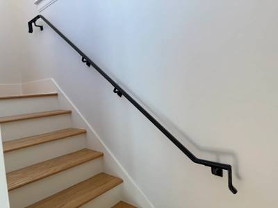Black wall handrail with returned ends beside pale wooden stairs