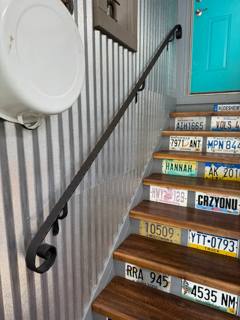 Black wall-mounted handrail beside indoor wooden stairs with colorful riser signs