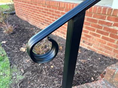 Close-up of a curled handrail end beside a brick porch