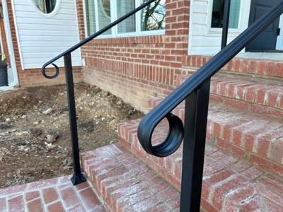Close-up of curled black handrail ends beside brick steps