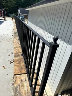 Close view along a black picket railing beside pale vertical siding