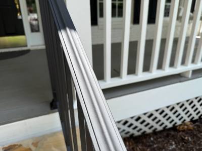 Close view along a ridged black handrail beside a white porch railing