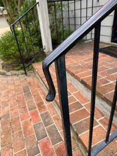 Close view of a black stair handrail with a curled end above brick paving