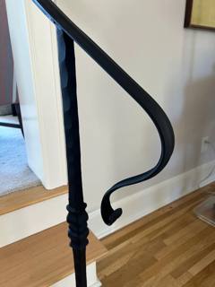 Close view of a curled black handrail return above a decorative stair post