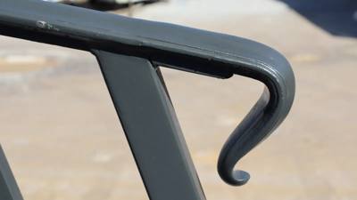 Close view of a curled black handrail return against a pale paved background