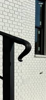 Close view of a curved black railing end against a white brick wall