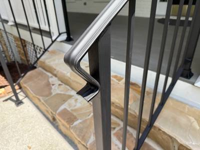 Close view of a shaped black handrail return beside a stone entrance landing