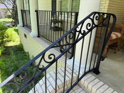 Close view of flowing scrollwork along a black porch stair railing