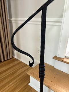 Curled black handrail end and decorative post beside wooden interior steps