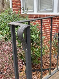 Curled handrail end above a narrow railing panel beside a brick porch