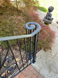 Curled top of a decorative railing beside a brick garden path