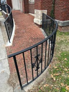 Curved black railing with decorative motifs along a brick entrance terrace