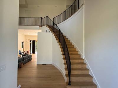 Curved wooden staircase with slender black balusters and an upper landing railing
