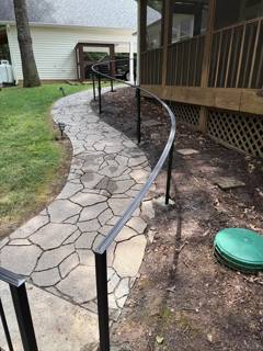 Curving black handrail following a stone garden path beside a wooden porch