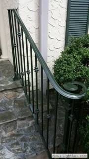 Dark green ornamental stair railing beside stone paving and white columns