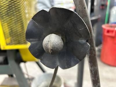 Dark sculpted metal flower with a textured round center in the workshop