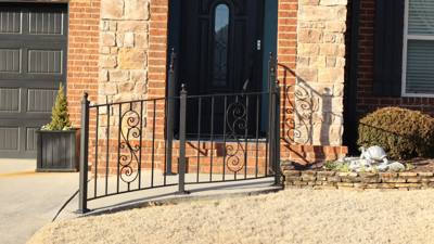 Decorative black entrance railings with scrollwork beside a brick doorway