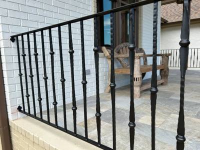 Decorative black porch railing beside white brick and outdoor chairs