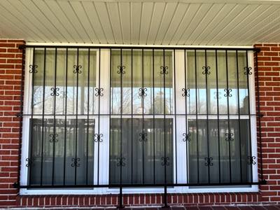 Decorative black window grilles covering a wide window in a brick wall