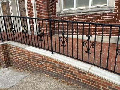 Decorative scroll accents in a long black railing above a brick porch wall