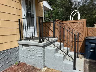Diamond-pattern black railing beside gray masonry steps and a privacy fence