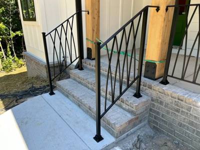 Diamond-pattern black stair railings beside pale brick steps and timber posts