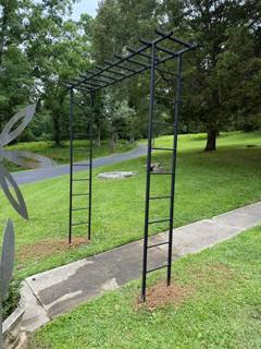 Freestanding black metal garden arbor spanning a concrete path