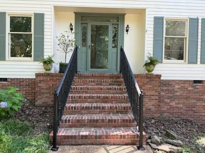 Front view of black railings flanking brick steps at a pale-sided house