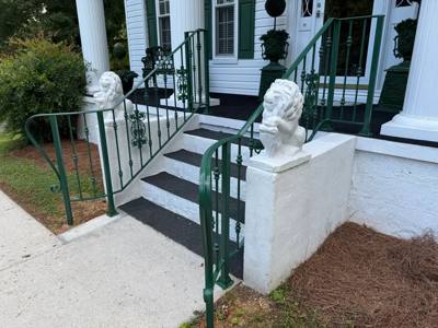 Green-painted handrails beside white porch steps and decorative lion figures