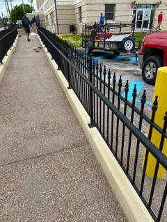 Long black spear-top fence separating a sidewalk from parked vehicles