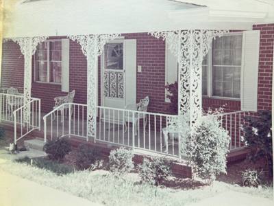 Older photograph of white decorative porch supports beside brick entry steps