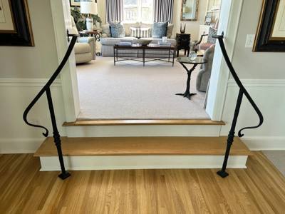 Paired black handrails with curled ends on a short wooden interior stairway