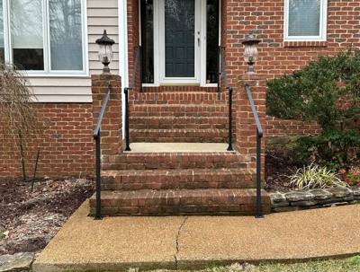 Paired simple black handrails flanking brick steps at a front door