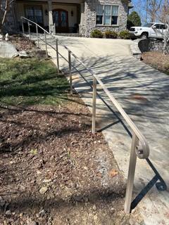 Pale handrail following an outdoor path toward a driveway