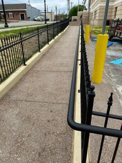 Paved ramp bordered by black handrails and spear-top fencing