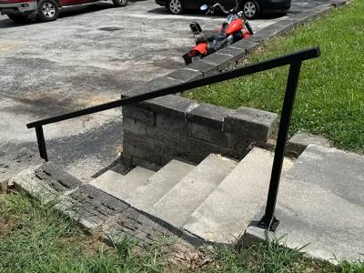 Plain black handrail descending beside concrete steps and a block retaining wall