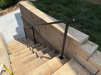 Plain black handrail descending concrete steps beside a block retaining wall