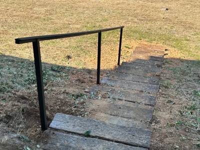 Plain black handrail following a short stone path through a lawn