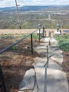 Plain black handrail following a stone garden path toward a distant view