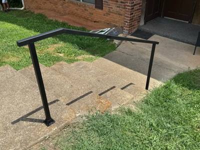 Plain black handrail following concrete steps beside a brick corner