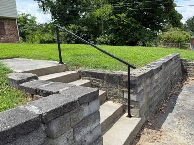 Plain black handrail following concrete steps through a block garden wall