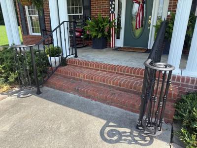 Scroll-end black railings beside a brick porch and white columns