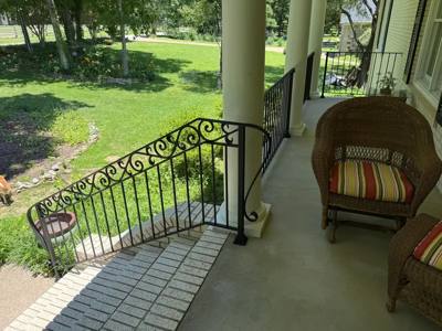 Scroll-pattern black stair railing beside a shaded front porch