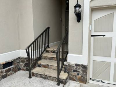 Short black handrails beside rough stone steps at a recessed entrance