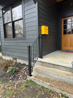 Short black picket railing beside concrete steps at a gray-sided entrance