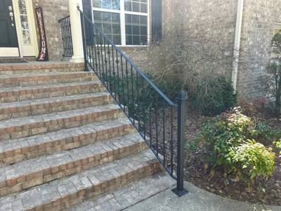 Side view of a decorative black railing beside pale brick steps and shrubs