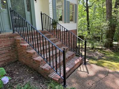 Side view of black decorative railings beside brick entrance steps and trees
